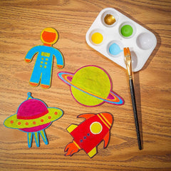 Colorful space-themed cutouts on a wooden surface with a paint palette and brush.