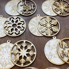 Wooden Christmas ornaments with snowflake designs and 'Let It Snow' text on a wooden surface.