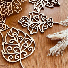 Decorative leaf cutouts on a wooden surface with dried pampas grass.