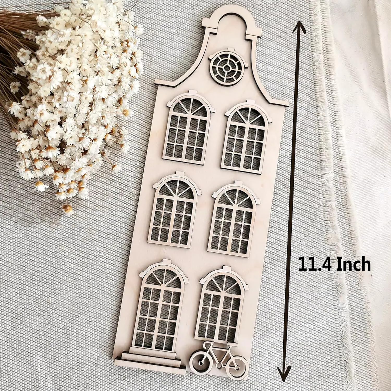 Decorative wooden cutout with window design and bicycle illustration on a textured surface with white flowers.