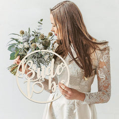 Woman holding a bouquet with a 'Bride to be' sign on a plain background