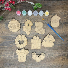 Wooden Christmas ornaments on a wooden surface with paint colors and a brush.