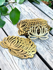 Three leaf-shaped coasters on a wooden surface with green leaves in the background