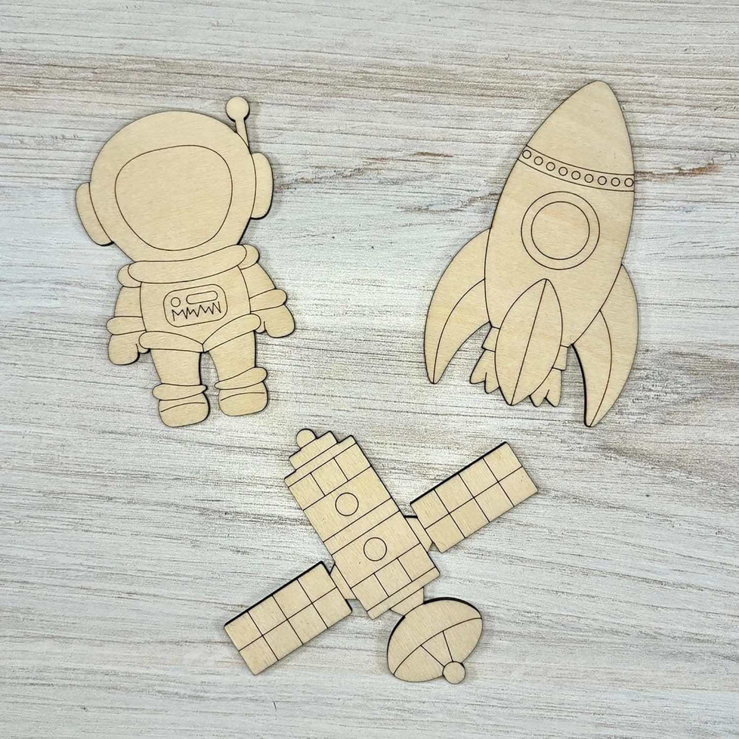 Wooden cutouts of an astronaut, rocket, and spaceship on a wooden surface