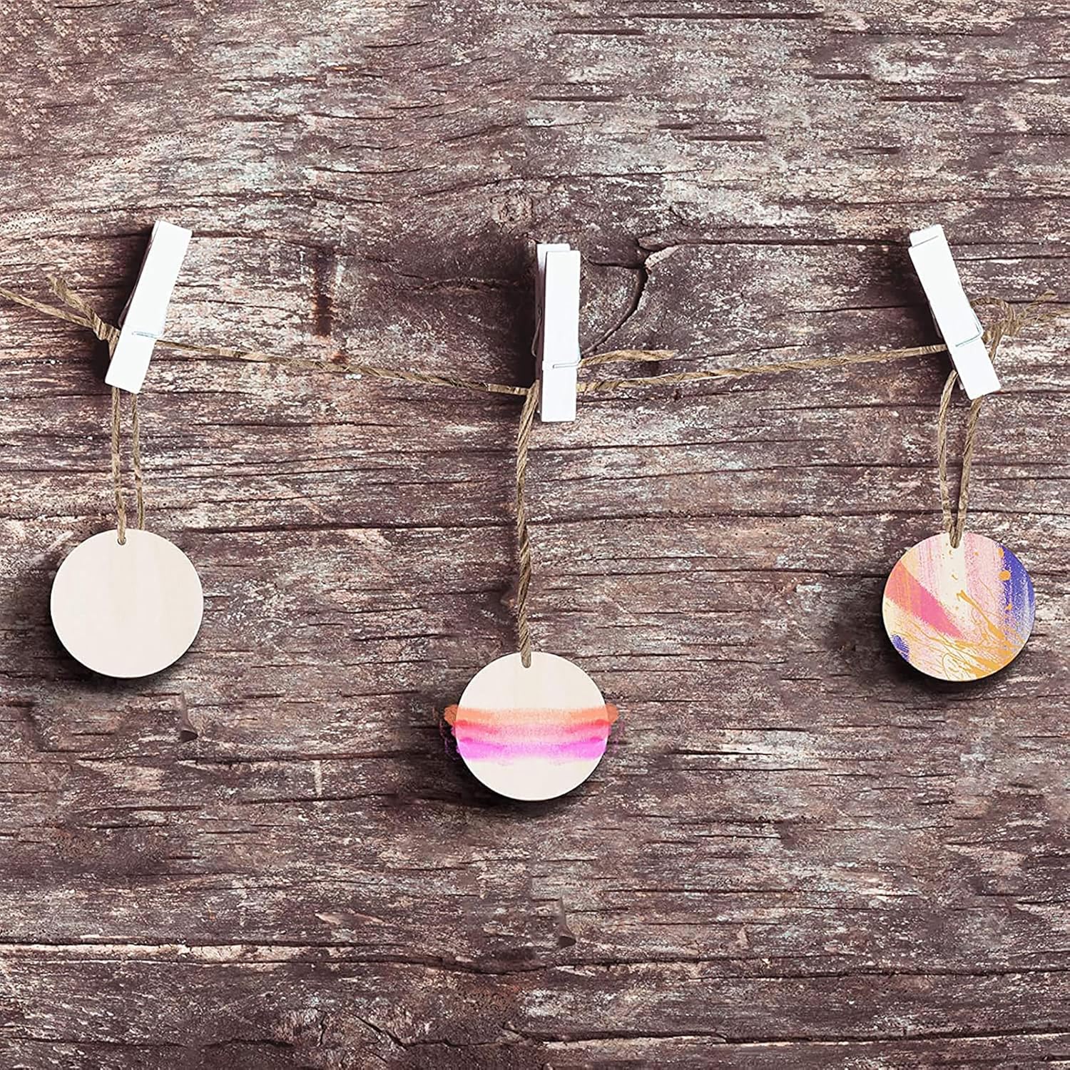 Decorative round ornaments with watercolor designs hanging on a string against a wooden background.