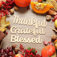 Autumn-themed arrangement with pumpkins, leaves, and 'Thankful Grateful Blessed' sign on a wooden surface.