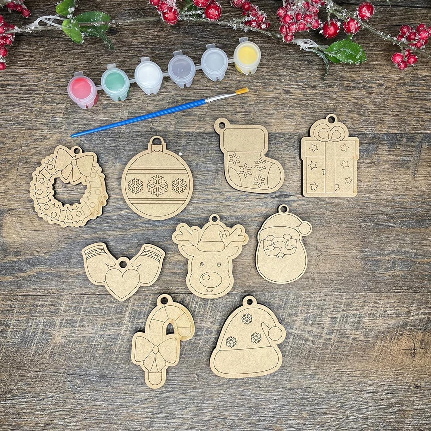 Wooden Christmas ornaments on a wooden surface with paint containers and a brush.