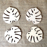 Four white leaf-shaped coasters with black patterns on a textured beige background