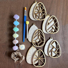 Geometric wooden wall hangings with paintbrushes, paint, and twine on a wooden surface