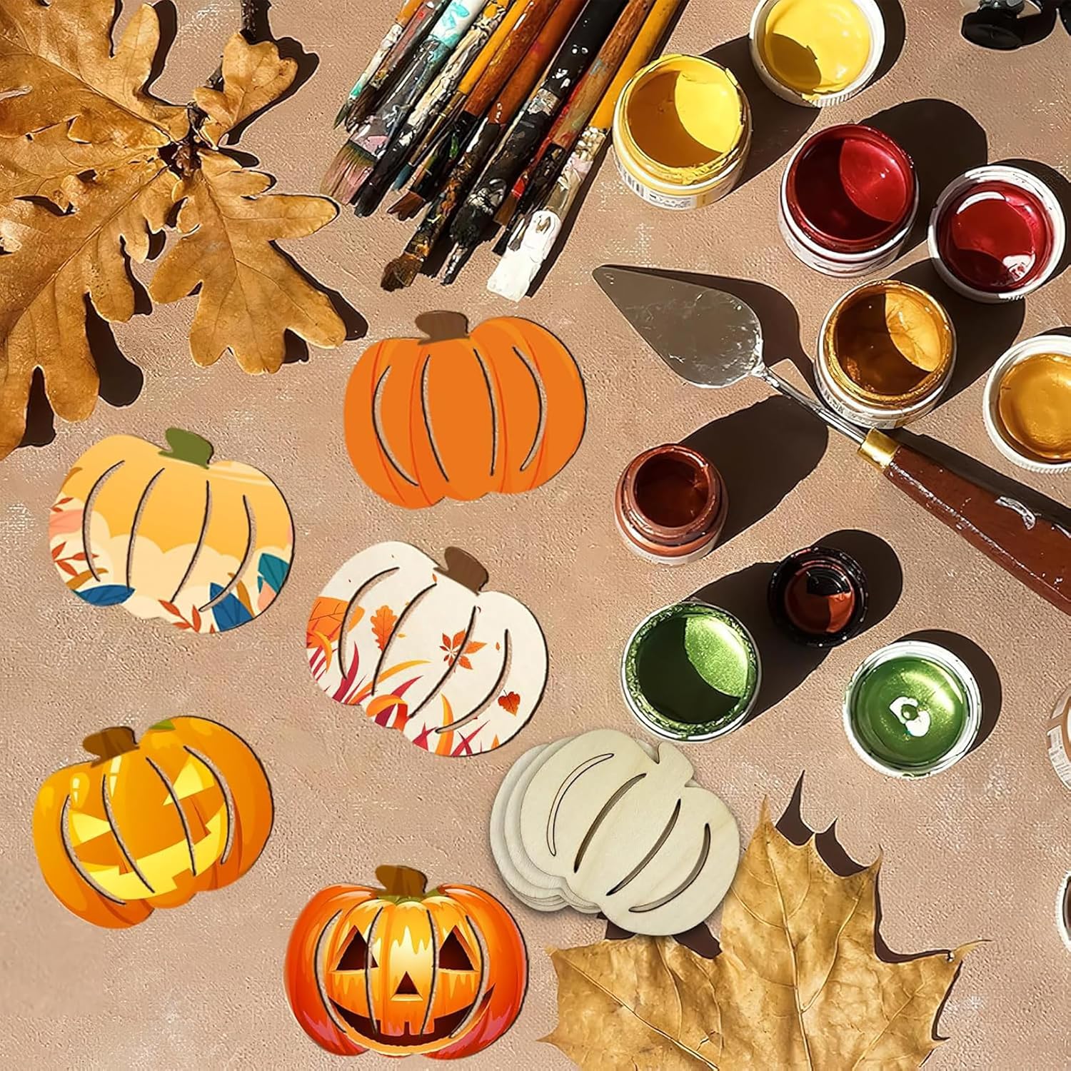Painting supplies including pumpkins, leaves, and paint jars on a beige surface.