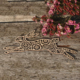 Decorative wooden hare with floral patterns on a rustic wooden surface with pink flowers.