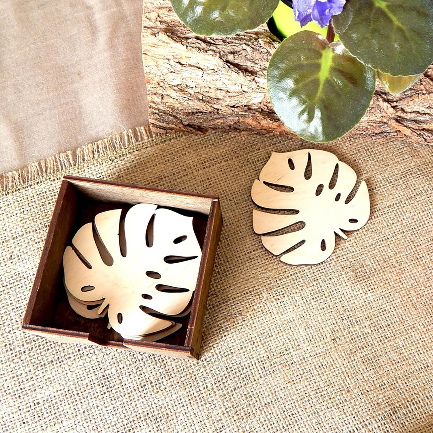 Wooden leaf-shaped coasters in a box on a textured surface with a leaf decoration in the background.