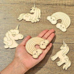Wooden unicorn and rainbow shapes on a wooden surface with a hand holding one of the shapes.