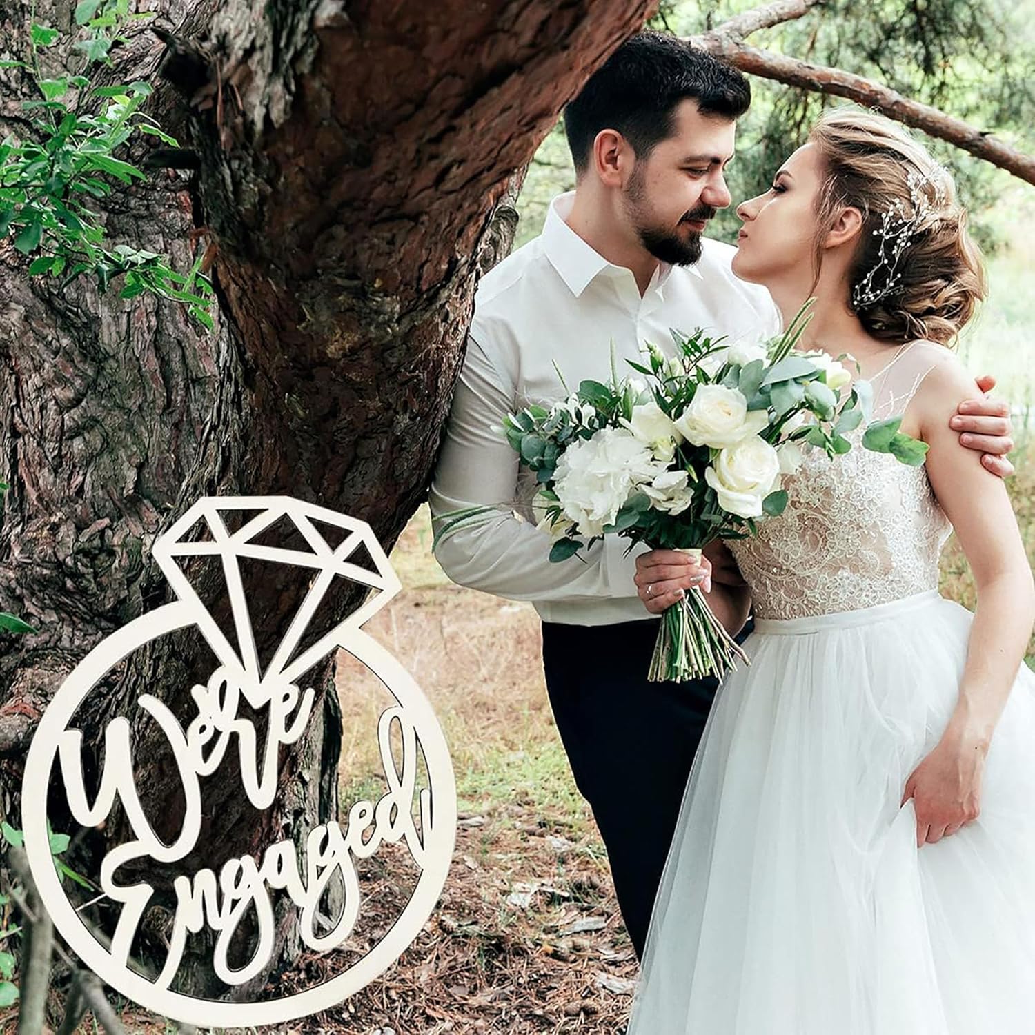 Engaged couple in a forest with 'We Are Engaged' sign.