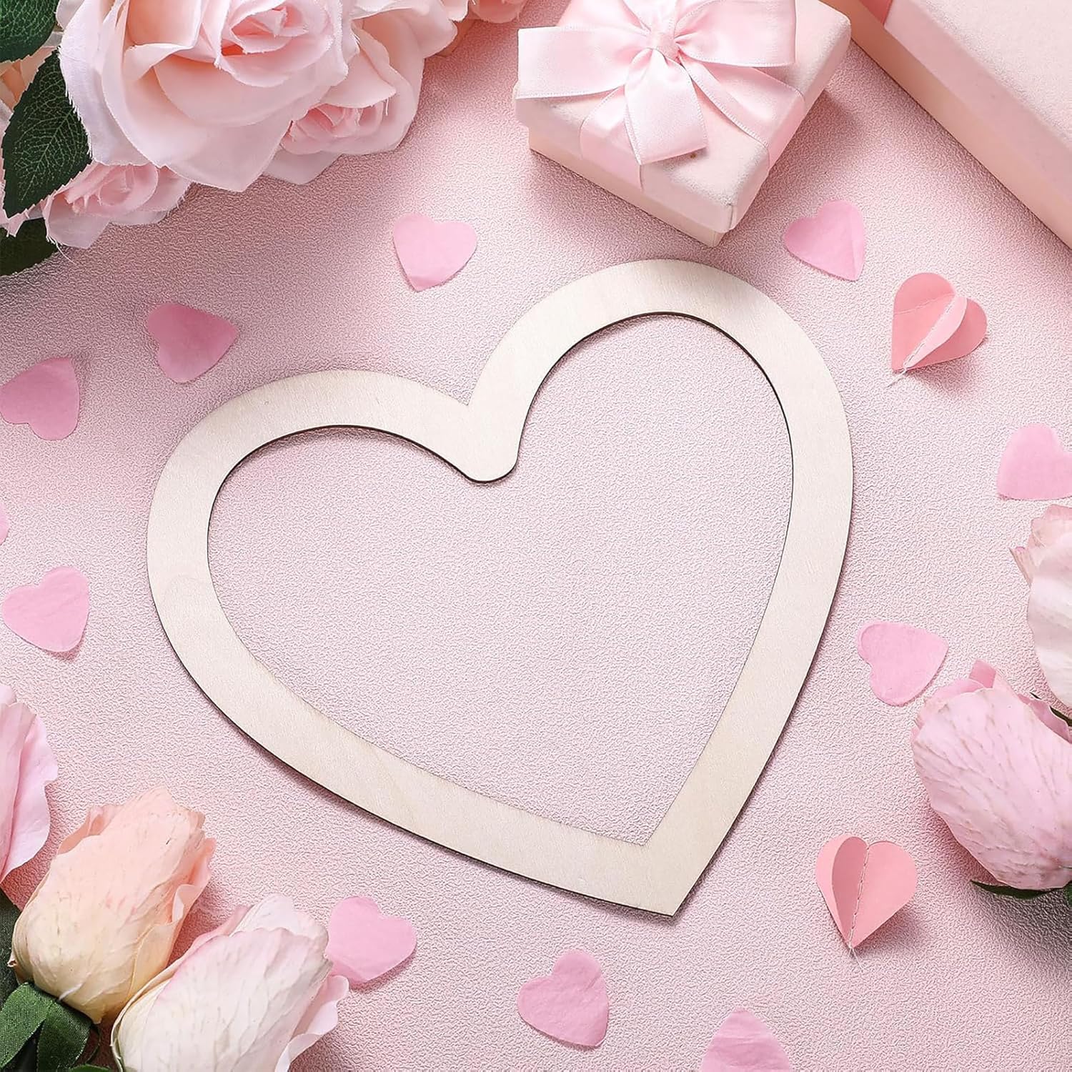 Heart-shaped frame surrounded by pink flowers and petals on a pink background