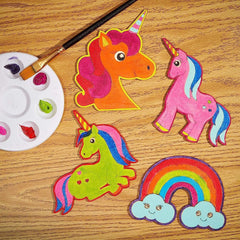 Colorful unicorn and rainbow craft items on a wooden surface with a paintbrush and palette.