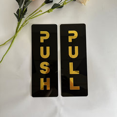 Two black rectangular signs with gold text 'PUSH' and 'PULL' on a white background.