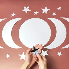 Hands holding a black star-shaped object against a pink background with white crescent moons and stars.