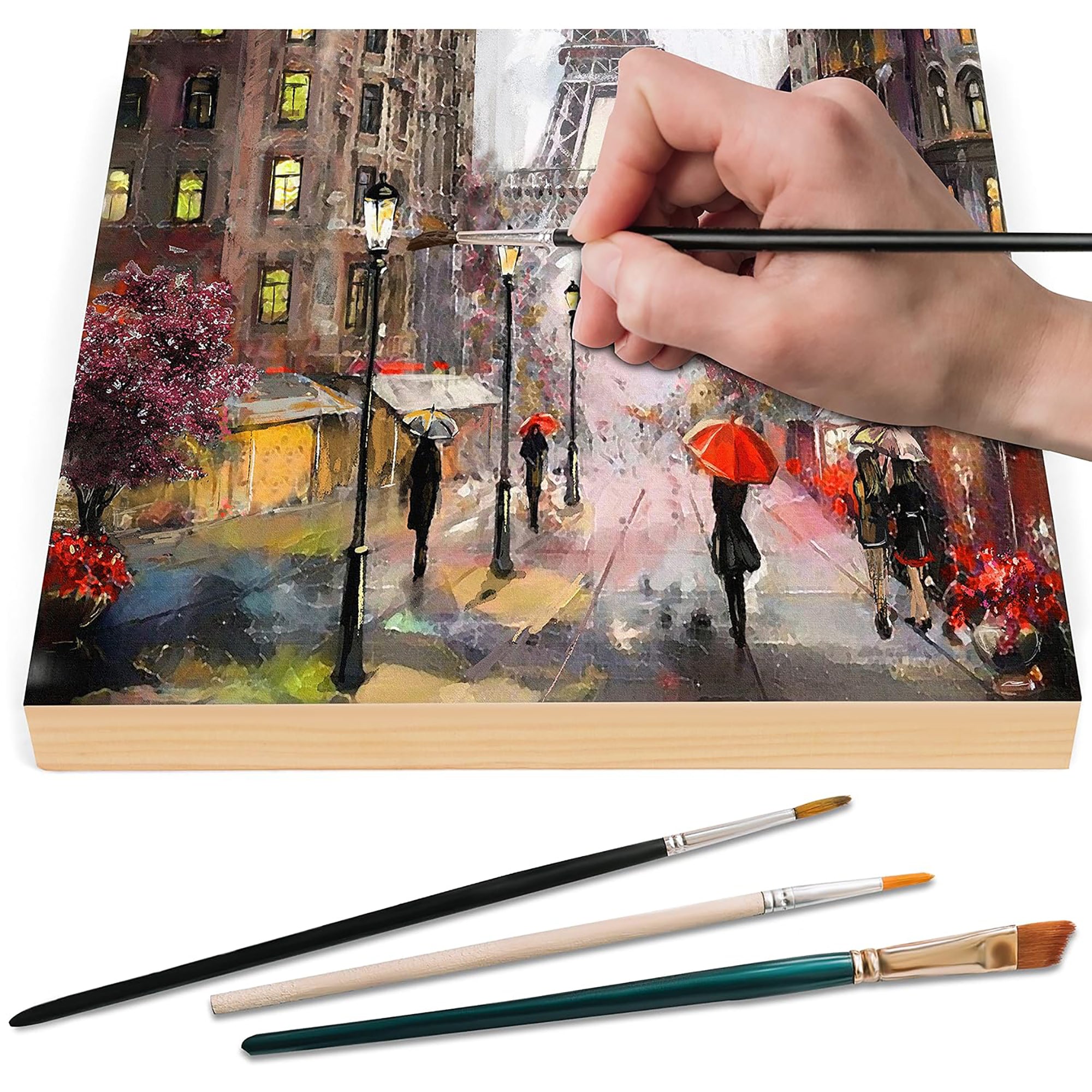 Painting of a city street scene with people and umbrellas, hand holding a brush, and three paintbrushes on a white background.