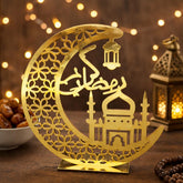 Decorative gold crescent moon with mosque silhouette on a wooden surface with blurred lights in the background.