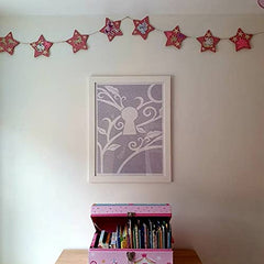 Children's room with pink star decorations, a toy chest, and framed artwork on a white wall.