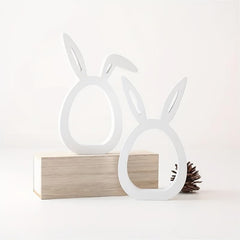 White rabbit-shaped lamps on a wooden block with a pine cone on a white background