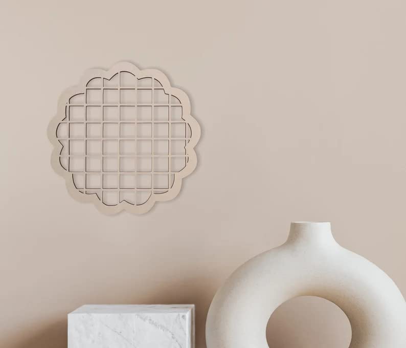 Decorative wall art piece on a beige wall with a white vase below.