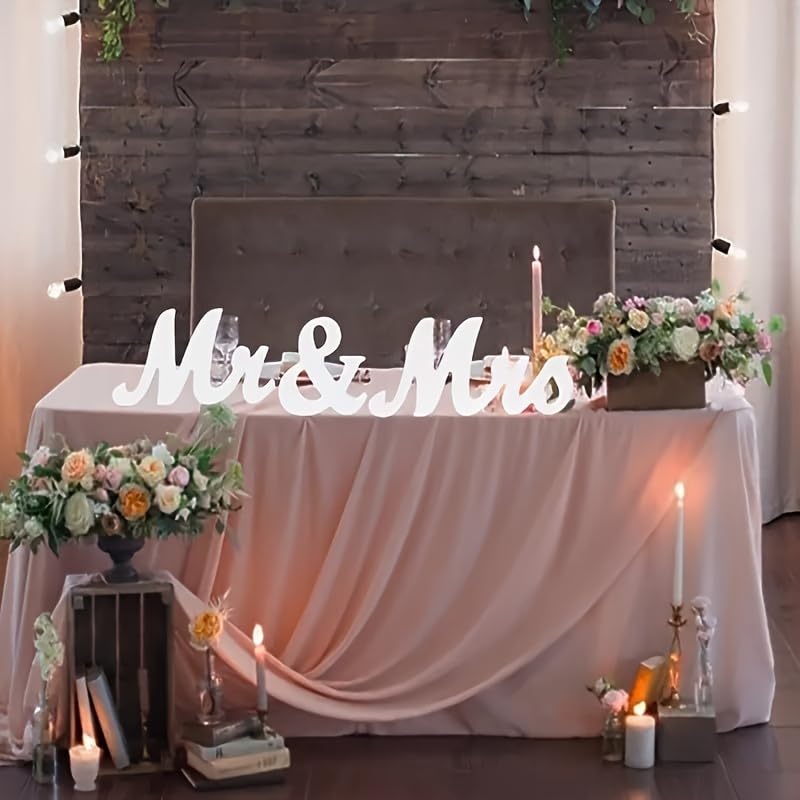 Decorated table with 'Mr & Mrs' sign, flowers, and candles against a wooden wall.