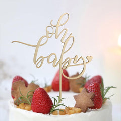 Gold 'oh baby' cake topper on a decorated cake with strawberries and cookies.