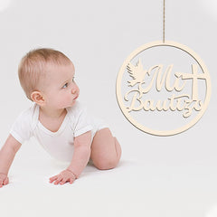Baby in a white onesie sitting on a white surface with a decorative circular sign with text hanging above.