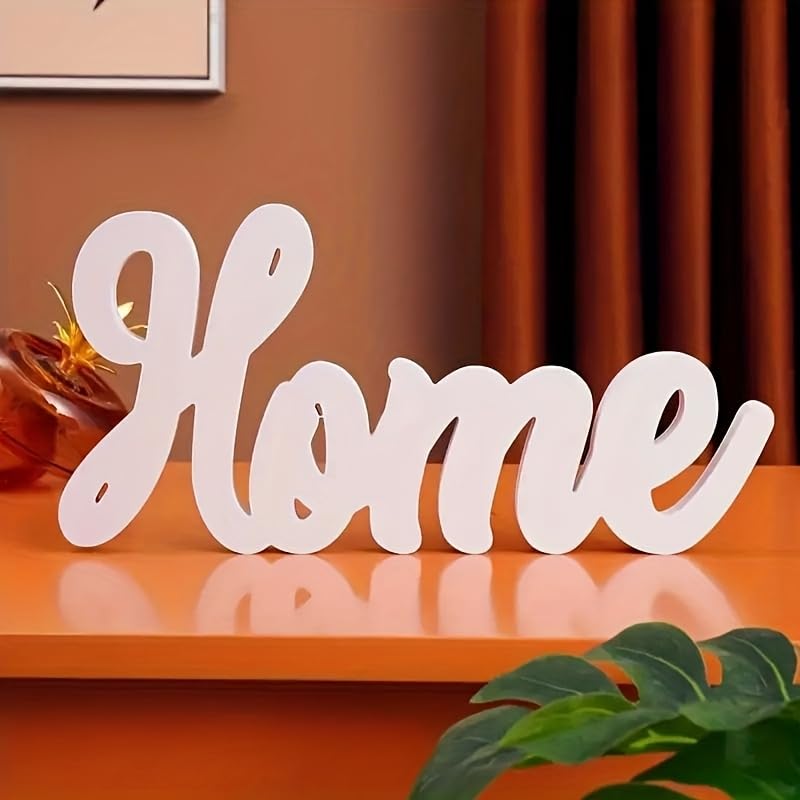 Decorative word 'Home' on a wooden shelf with a plant and framed picture in the background.