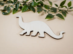 White wooden dinosaur toy on a beige background with green leaves