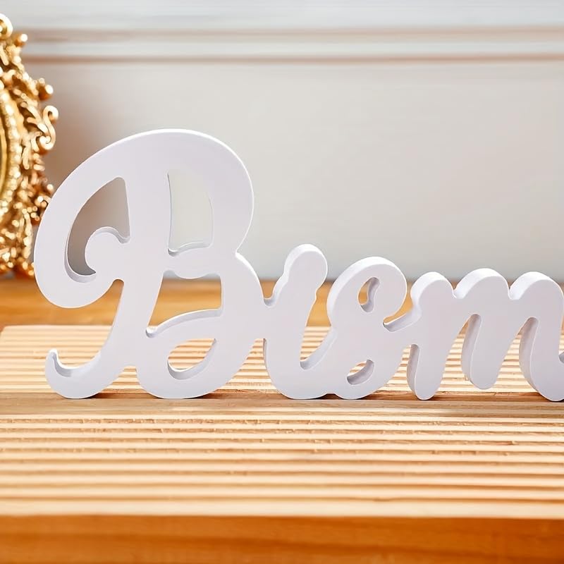 White decorative word 'Bless' on a wooden surface with a gold decorative item in the background.