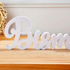White decorative word 'Bless' on a wooden surface with a gold decorative item in the background.