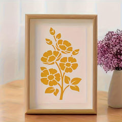 Framed artwork with yellow floral design on a light background, next to a vase with purple flowers.