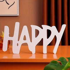 White decorative word 'HAPPY' on a wooden surface with a blurred background