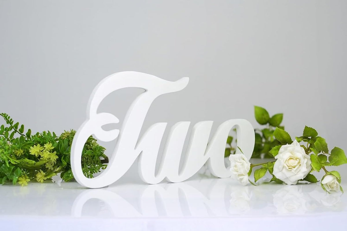 White decorative number 'Two' with greenery on a light gray background