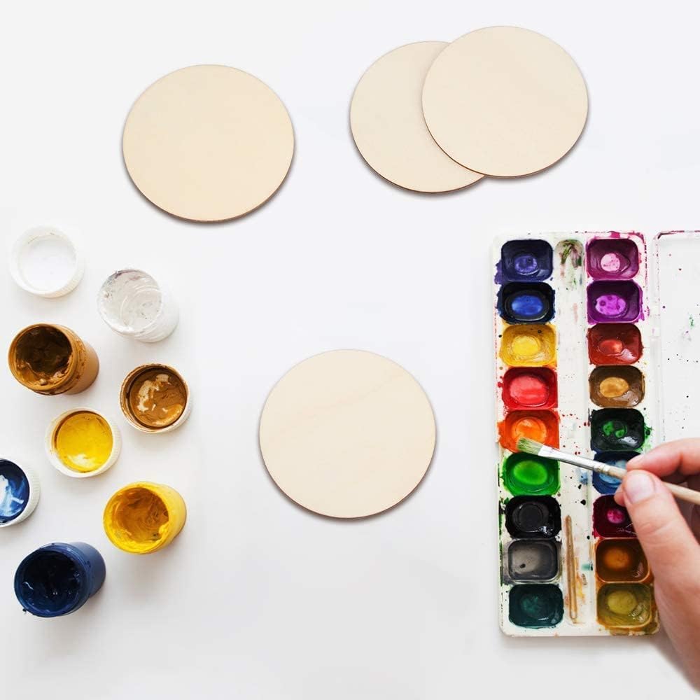 Art supplies including watercolor paints, brushes, and round canvases on a white surface.