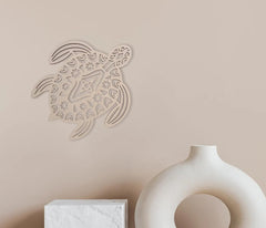 Decorative wall art of a turtle on a beige wall with a white vase and box below.