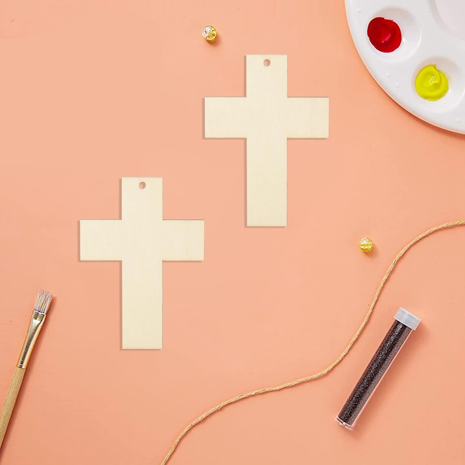 Wooden crosses on a peach-colored surface with paint supplies.