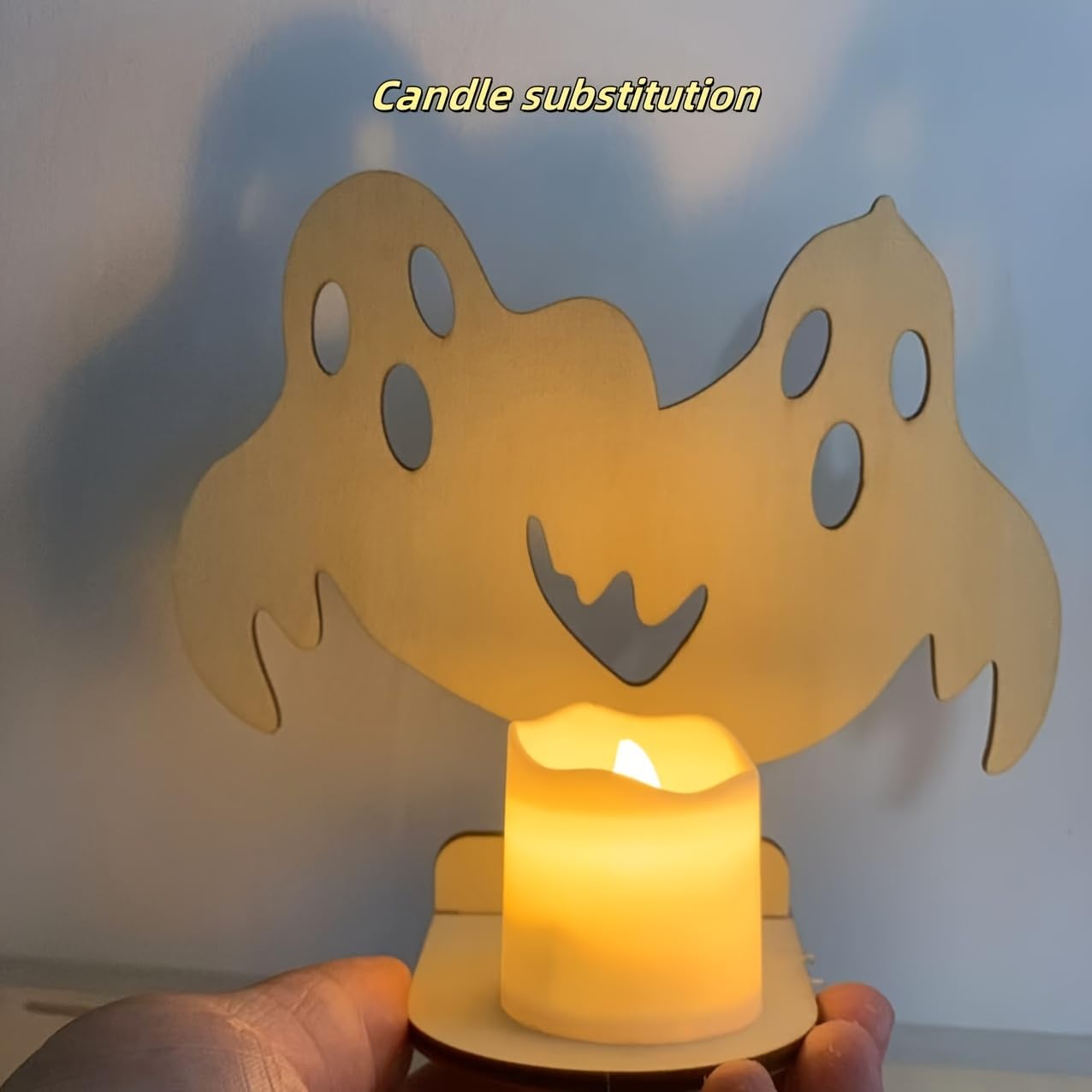 Ghost-shaped candle holder with a lit candle inside, against a plain background.