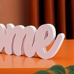 Pink decorative word 'Home' on an orange surface with a blurred background
