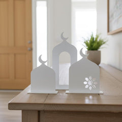 Decorative white metal lanterns with cut-out designs on a wooden surface.