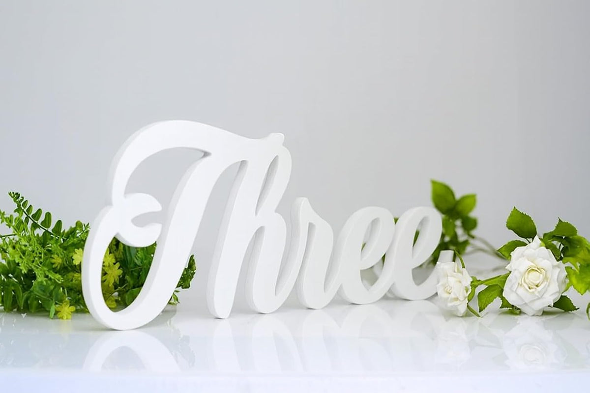 White decorative number 'Three' with greenery on a light gray background