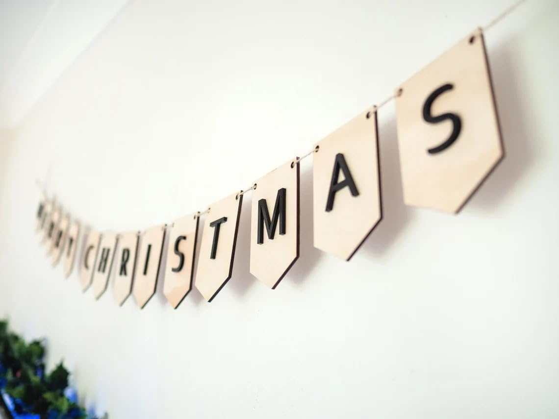 Christmas-themed banner with wooden letters spelling 'Merry Christmas' on a white wall.