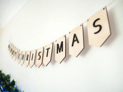 Christmas-themed banner with wooden letters spelling 'Merry Christmas' on a white wall.