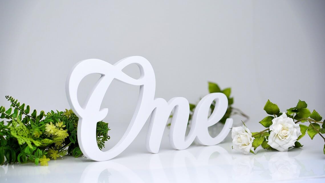 White decorative letter 'One' with greenery on a light gray background
