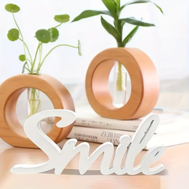 Decorative sign with 'Smile' on a surface with plants and books in the background