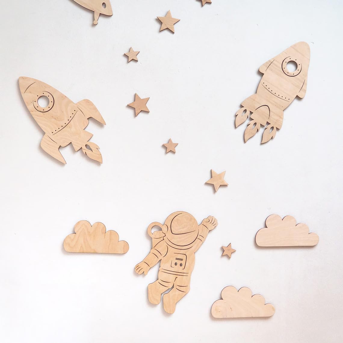 Wooden space-themed cutouts including rockets, stars, clouds, and an astronaut on a light gray background.