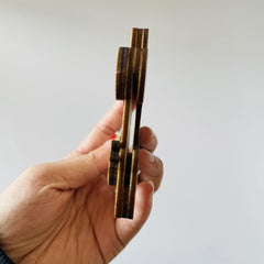 Hand holding a set of brass tongs against a plain background